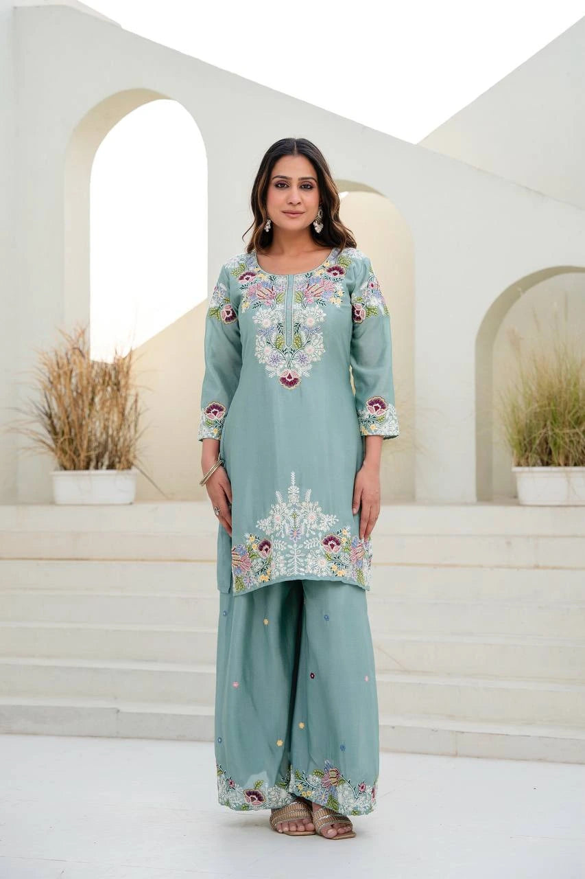 Woman wearing a light blue embroidered traditional outfit in an elegant setting.