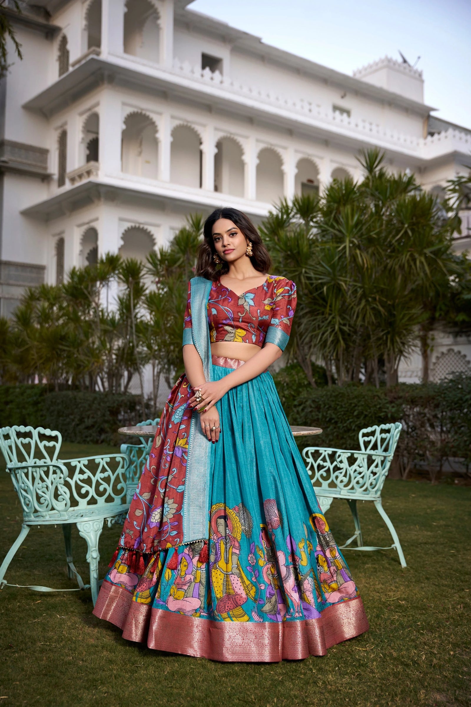Woman in a colorful traditional outfit standing in front of a white building with greenery.