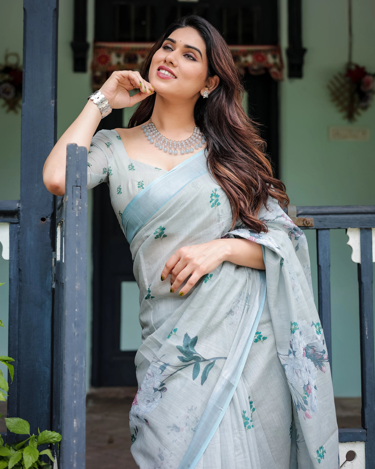 Woman wearing a light blue saree with floral patterns, holding a white card.