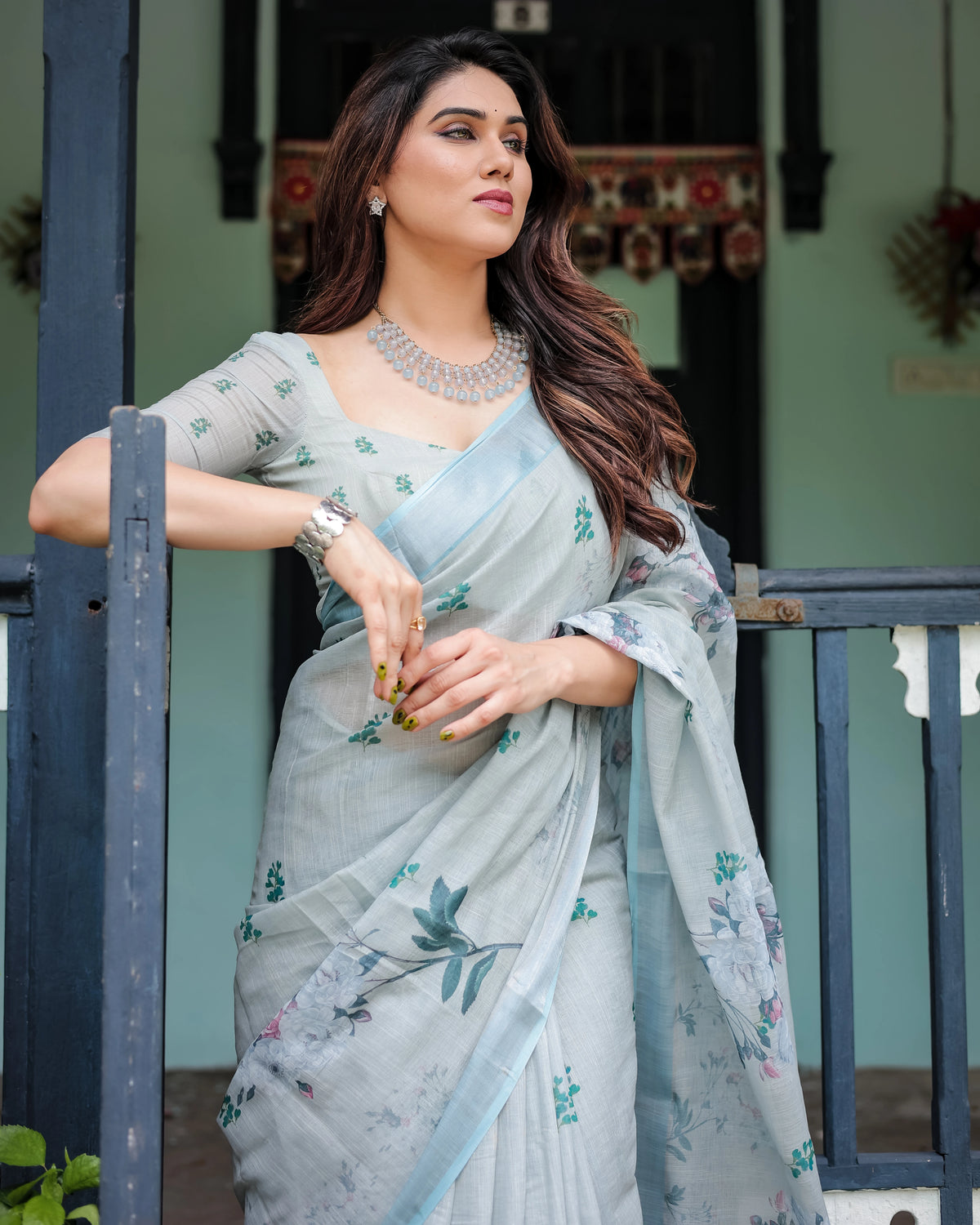 Woman in a light blue saree with floral patterns standing outdoors.