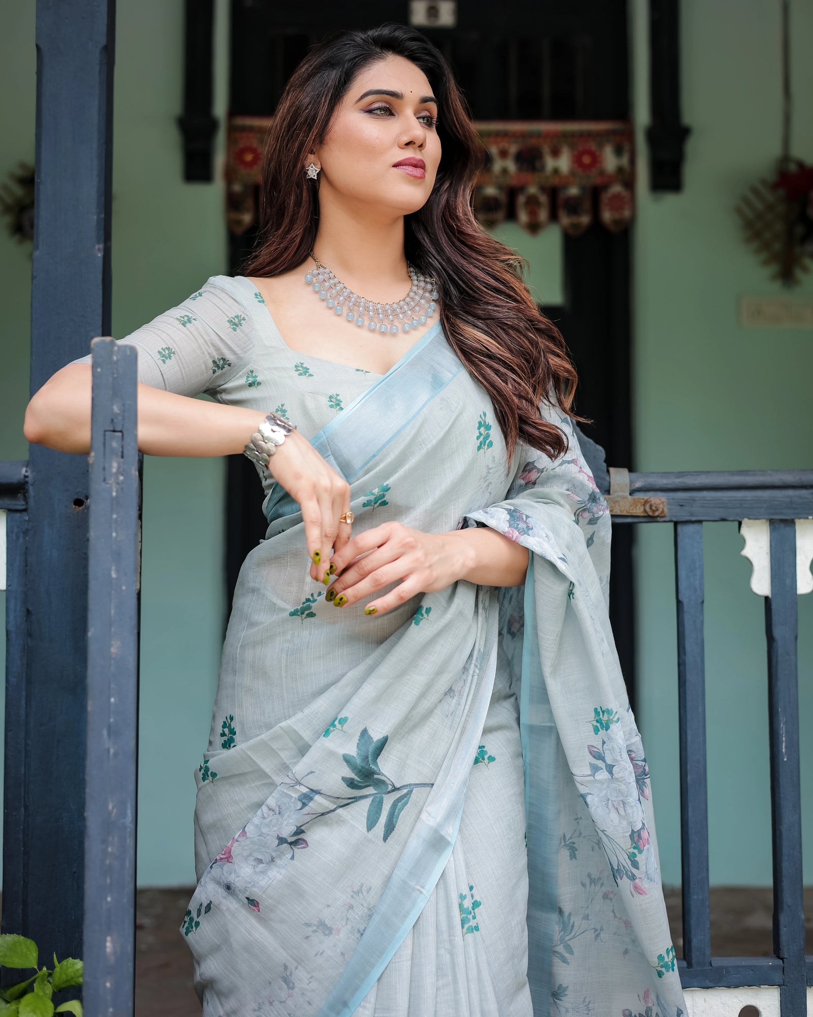 Woman in a light blue saree with floral patterns standing outdoors.