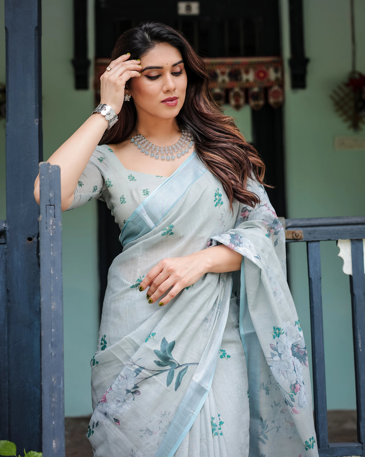 Woman in a light blue saree with floral patterns standing outdoors.
