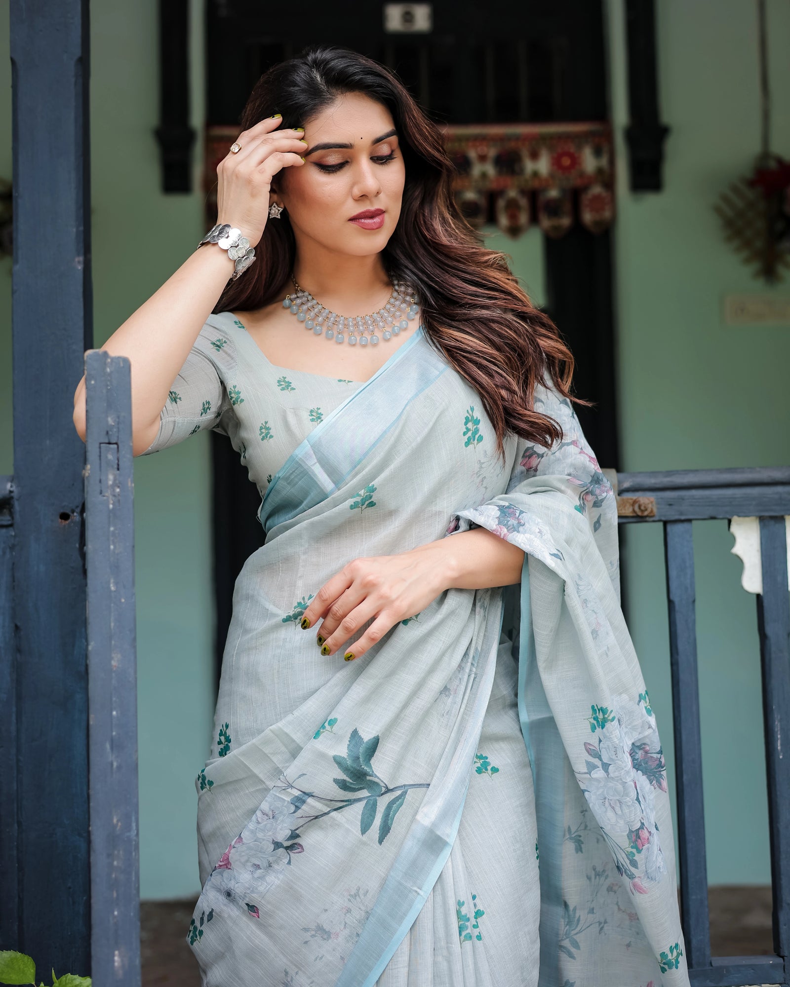 Woman in a light blue saree with floral patterns standing outdoors.