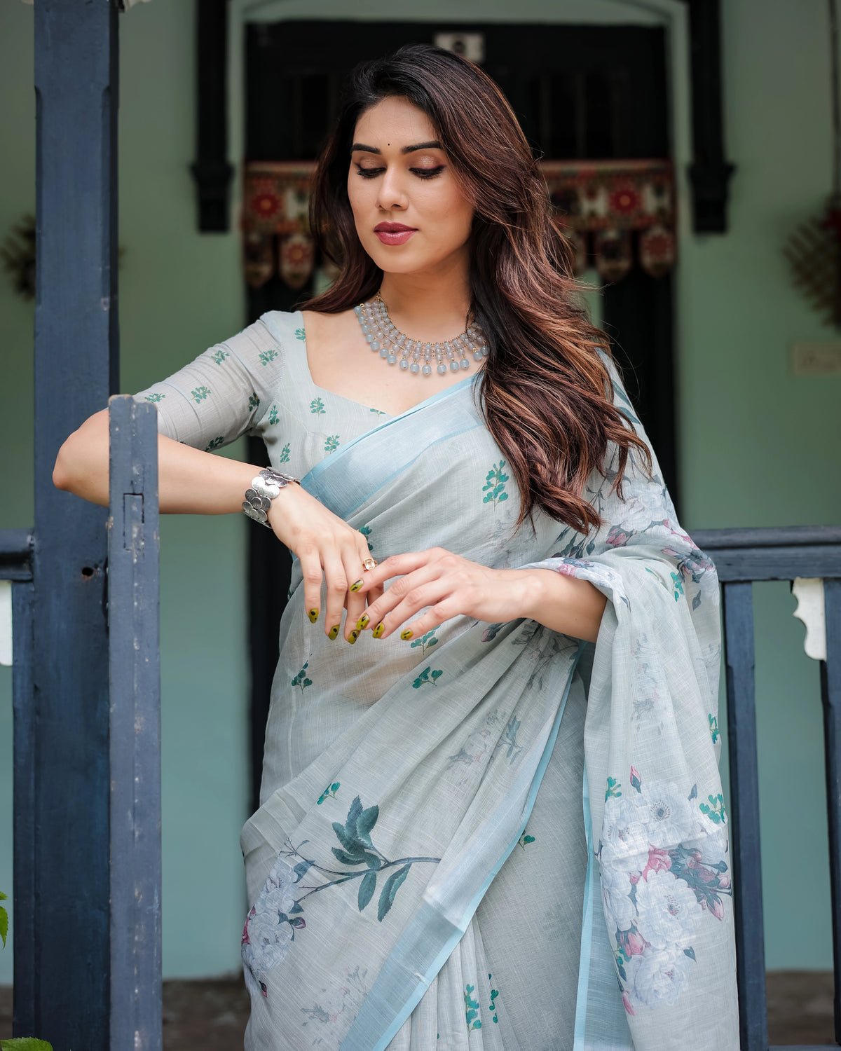 Woman in a light blue saree with floral patterns standing outdoors.