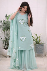 Woman wearing a light blue traditional outfit with floral patterns indoors.
