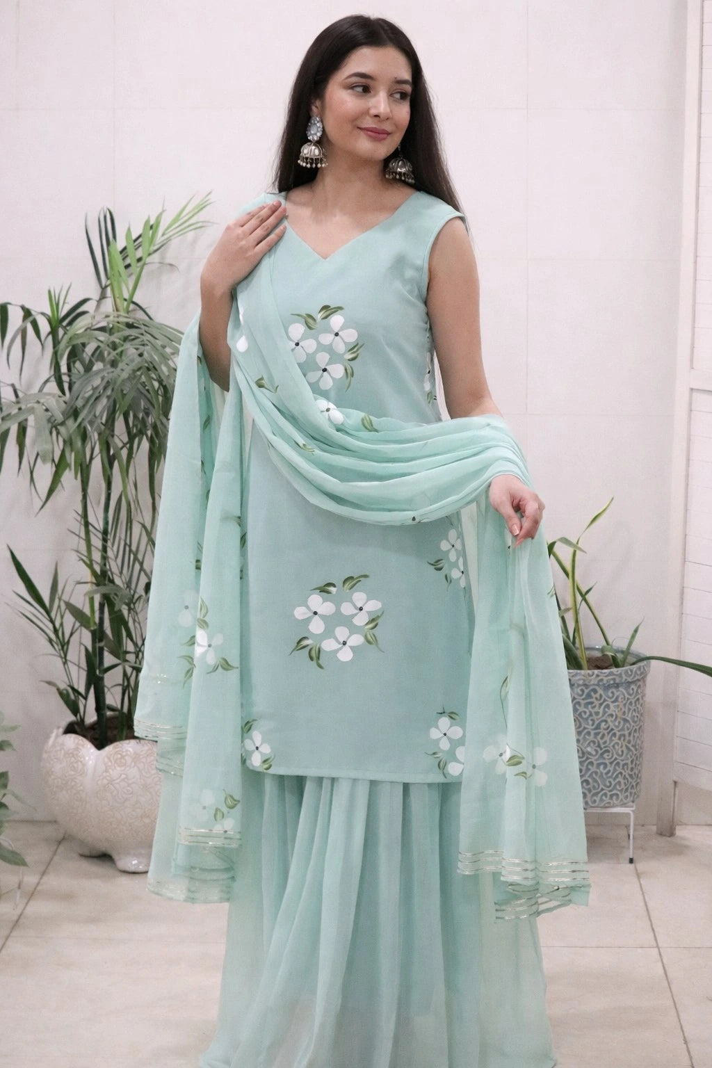Woman wearing a light blue embroidered dress with a matching dupatta in a minimal indoor setting.