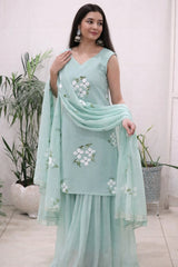 Woman wearing a light blue embroidered dress with a matching dupatta in a minimal indoor setting.