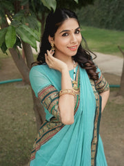 Woman in a turquoise saree with gold patterns standing outdoors.