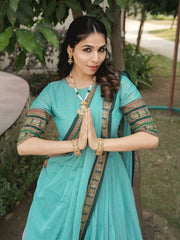 Woman in a traditional turquoise saree with gold patterns, standing outdoors.