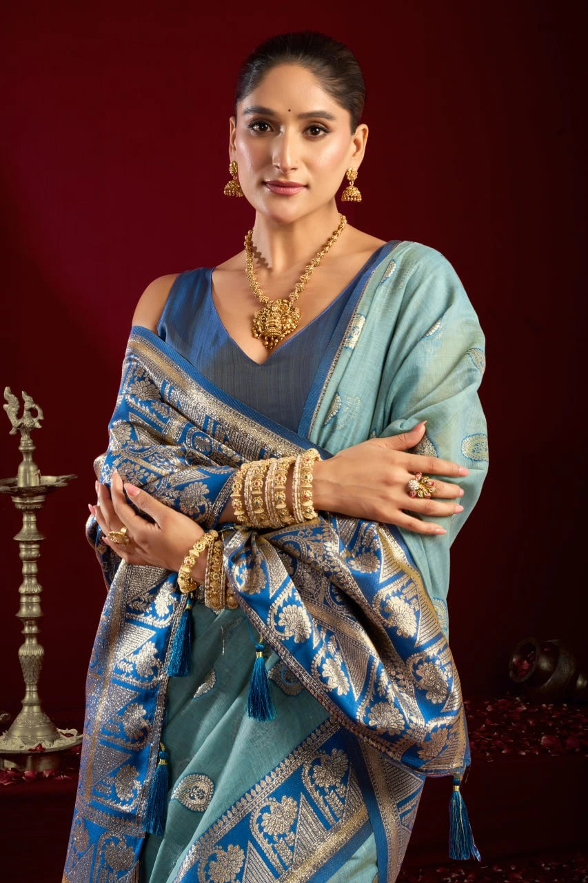 Woman in a traditional blue saree with gold jewelry against a dark red background