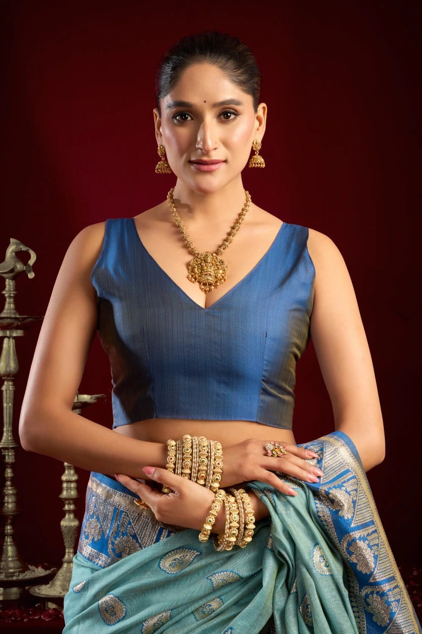 Woman in a blue saree with gold jewelry against a red background