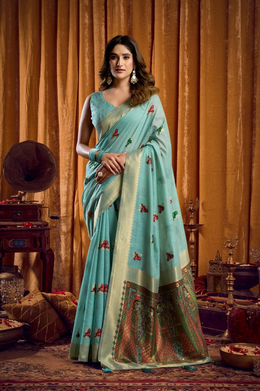 Woman in a light blue saree with floral patterns standing against an ornate backdrop.