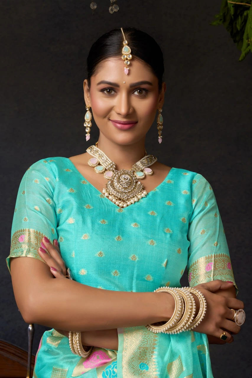 Woman in a teal saree with gold details and jewelry against a dark background