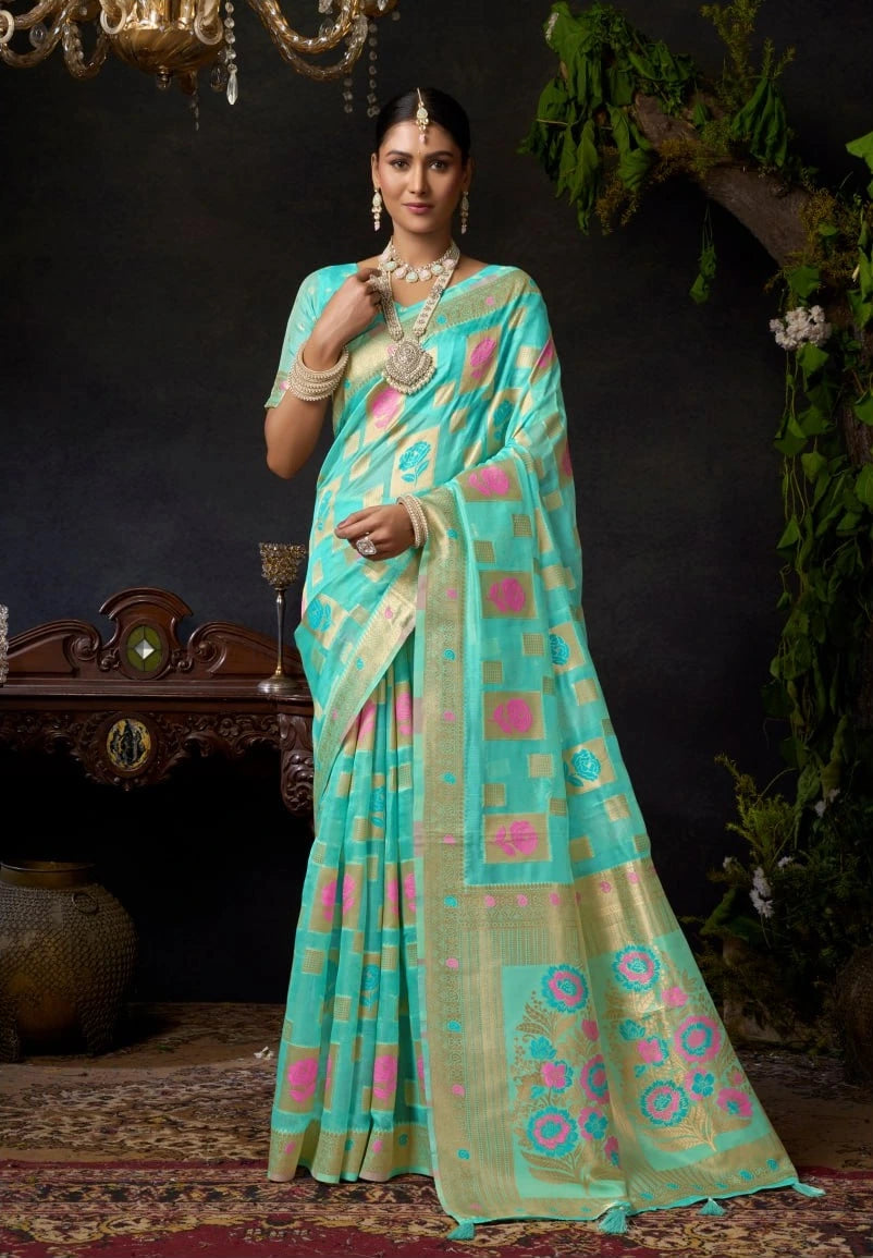 Woman wearing a light blue saree with pink patterns in a decorated indoor setting