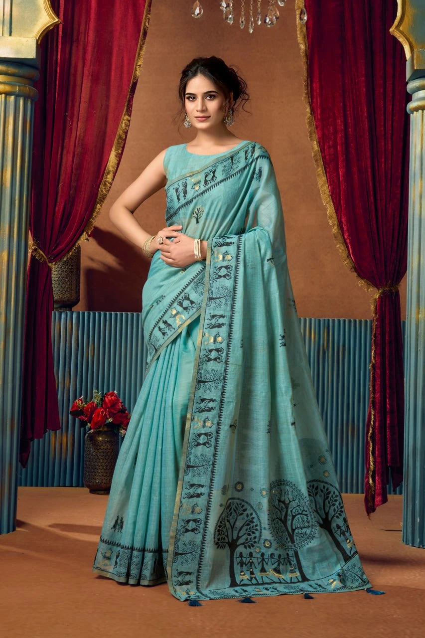 Woman wearing a light blue saree with a decorative pattern in front of red curtains.