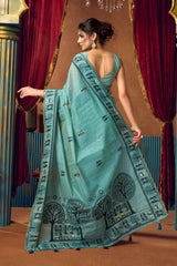 Woman wearing a light blue saree with black patterns in a decorative setting.