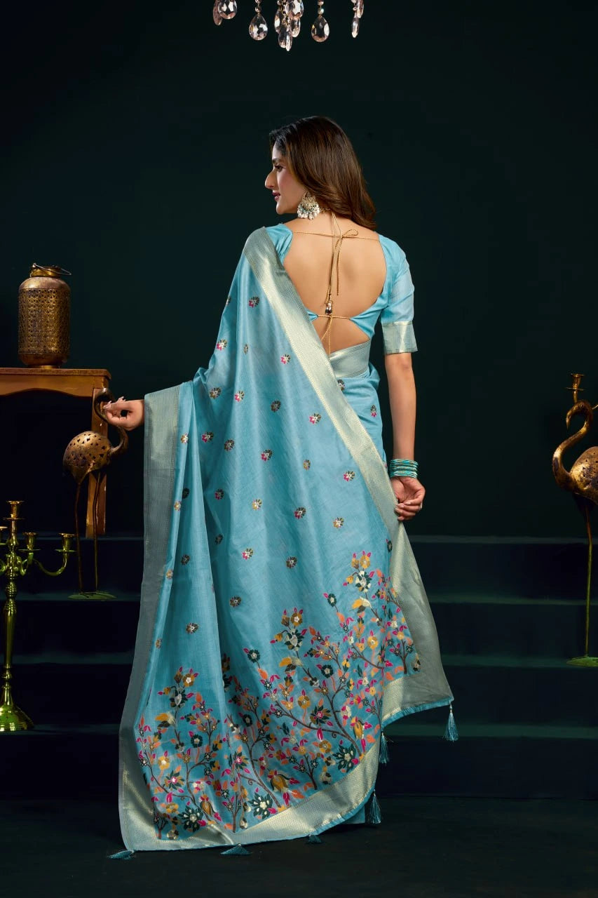 Woman in a light blue saree with floral patterns in a dark setting