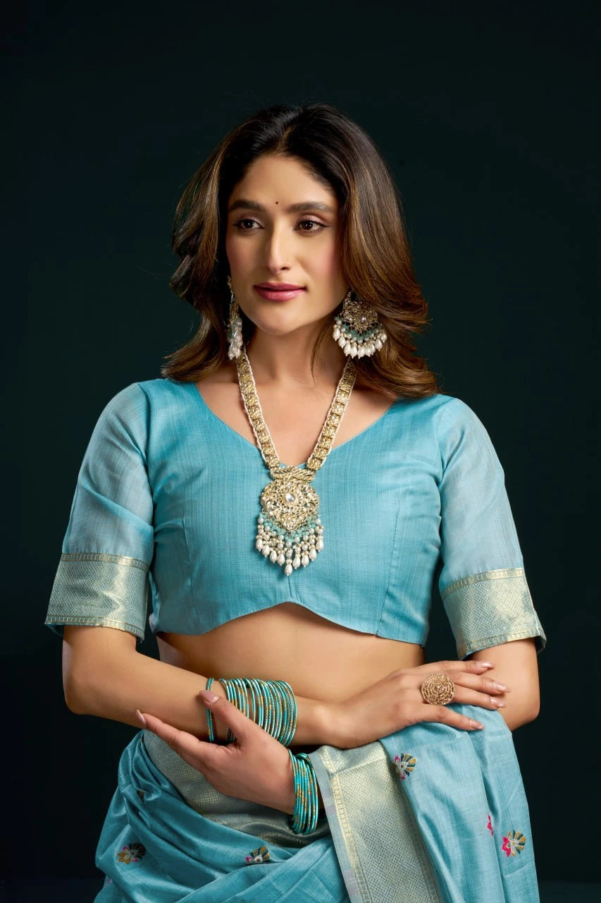 Woman in a light blue saree with jewelry against a dark background