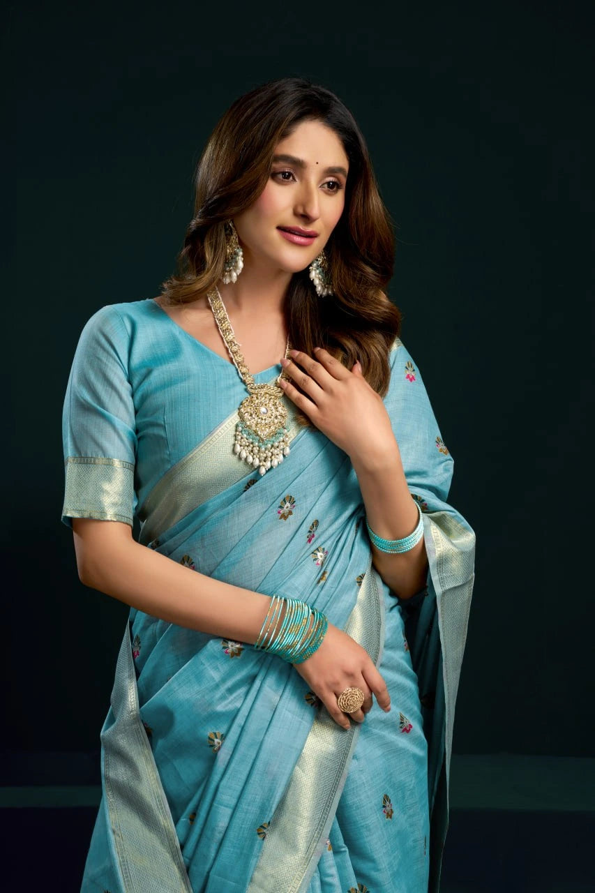 Woman in a light blue saree with silver border against a dark background