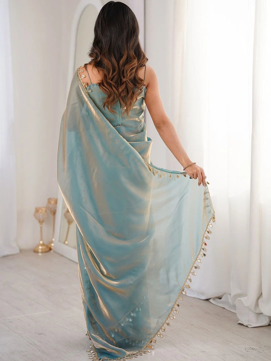 Woman wearing a light blue saree with gold trim in a minimalistic setting.