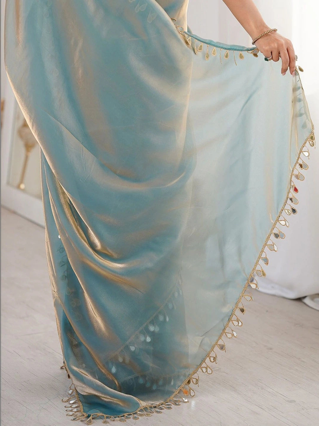 Light blue saree with gold trim being held by a person on a light wooden floor.