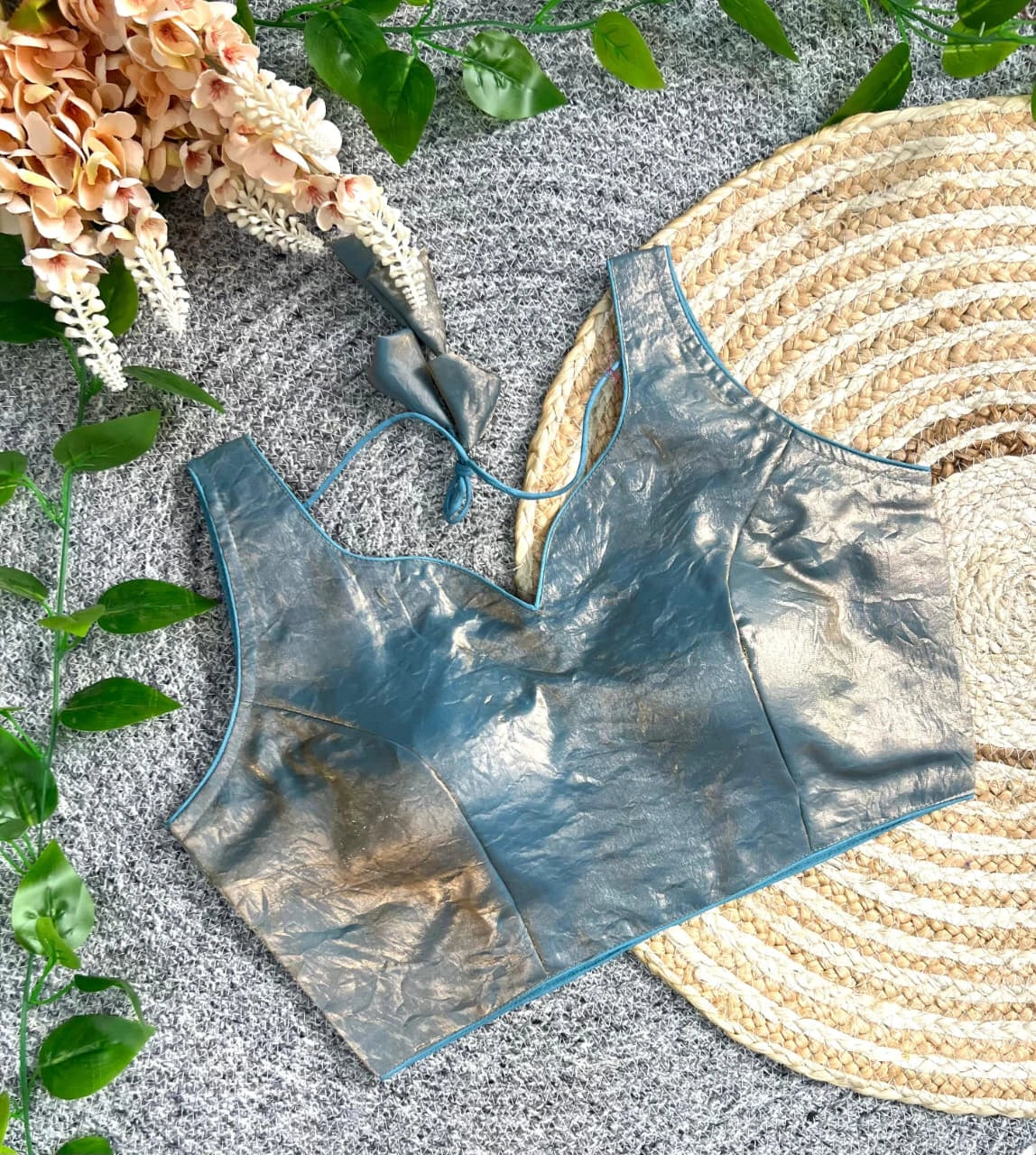 Blue metallic tank top on a textured surface with plants and a woven mat.