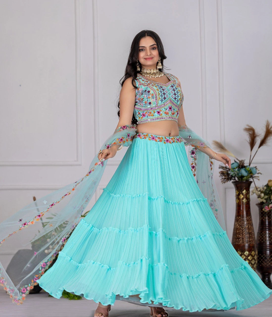 Woman wearing a light blue traditional outfit with floral details against a white wall.