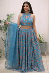 Woman wearing a blue floral outfit with a matching dupatta, standing indoors.