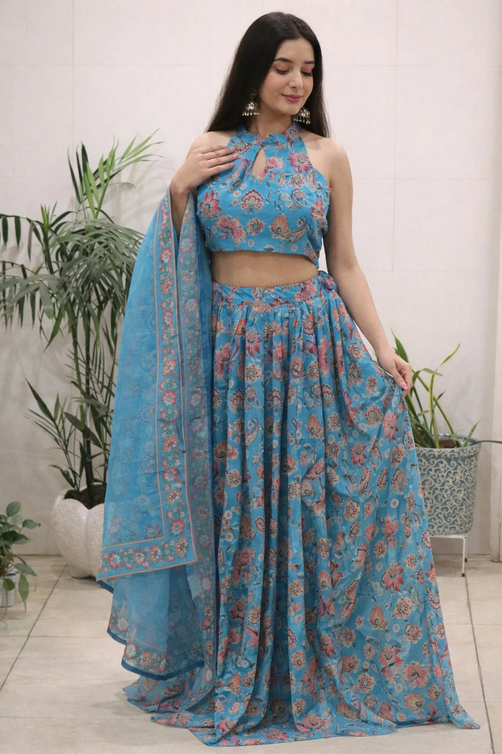 Woman wearing a blue floral traditional outfit with a matching dupatta in a minimal indoor setting.