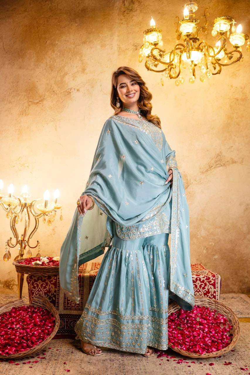 Woman in a light blue traditional outfit standing in a decorated room with chandeliers and rose petals.