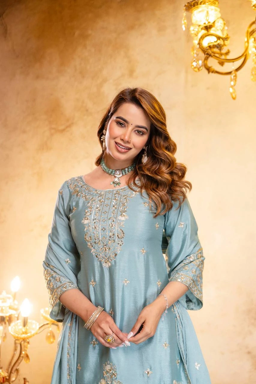 Woman wearing a light blue embroidered dress in a warmly lit room with chandeliers.