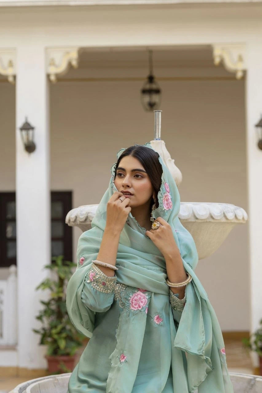 Woman in a light blue saree with floral patterns sitting outdoors.