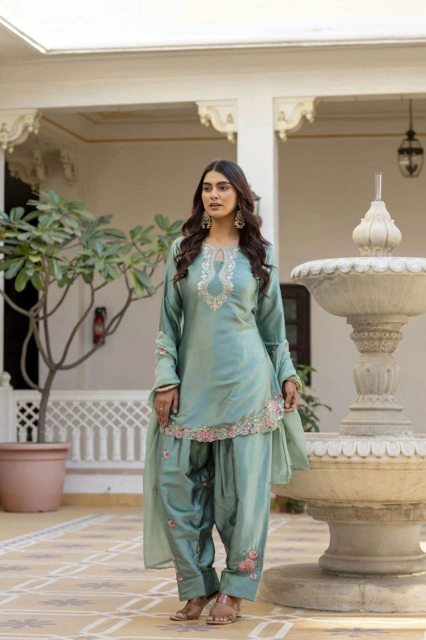 Woman in a light blue traditional outfit standing in an outdoor setting with a fountain.
