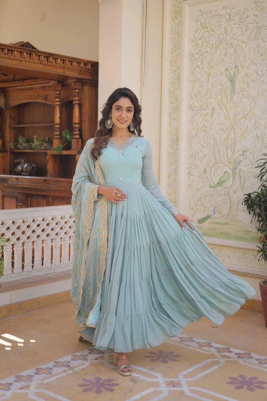 Woman in a light blue traditional outfit standing in an ornate room.