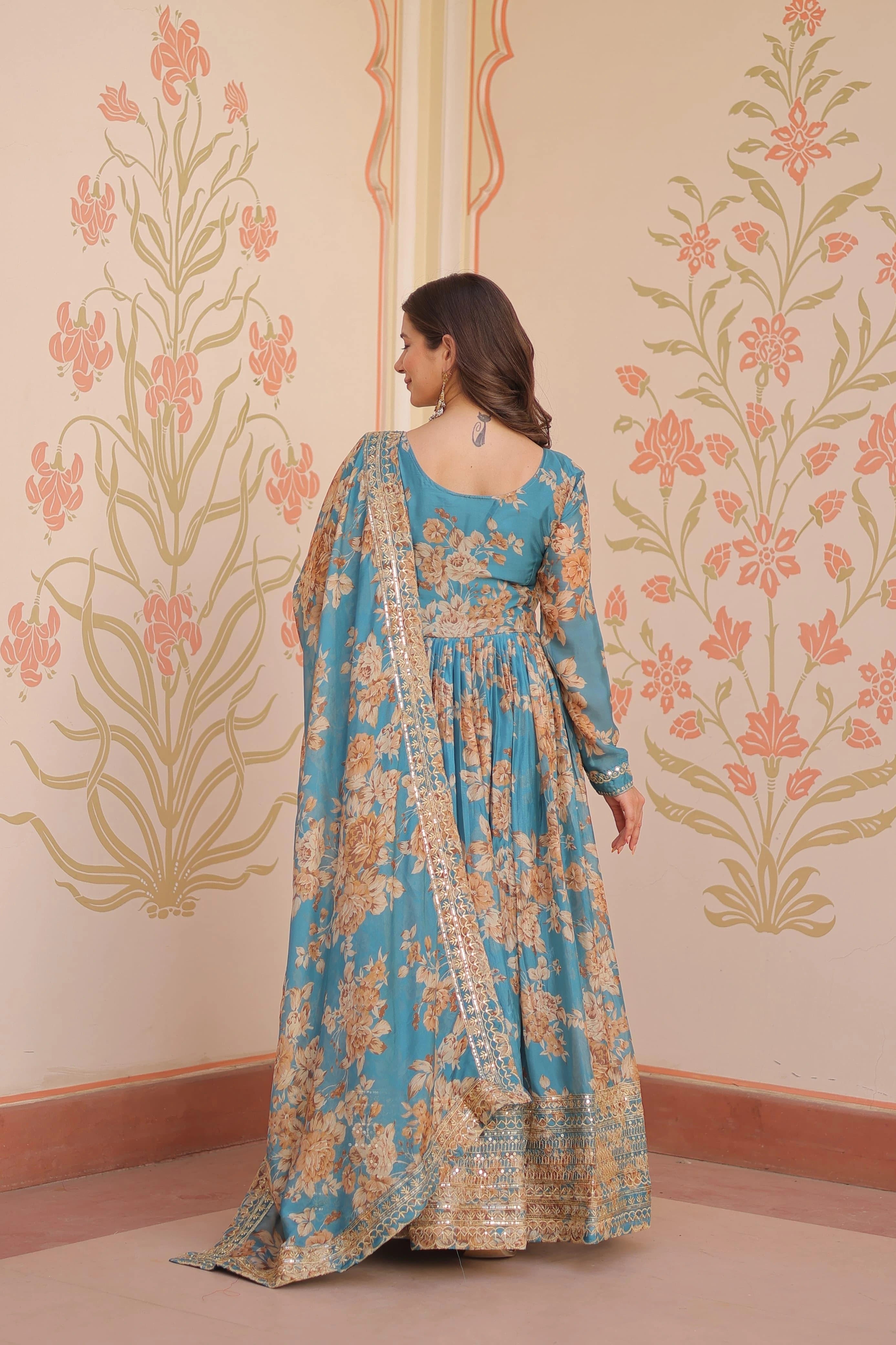 Woman in a floral dress standing against a decorative wall with floral patterns.