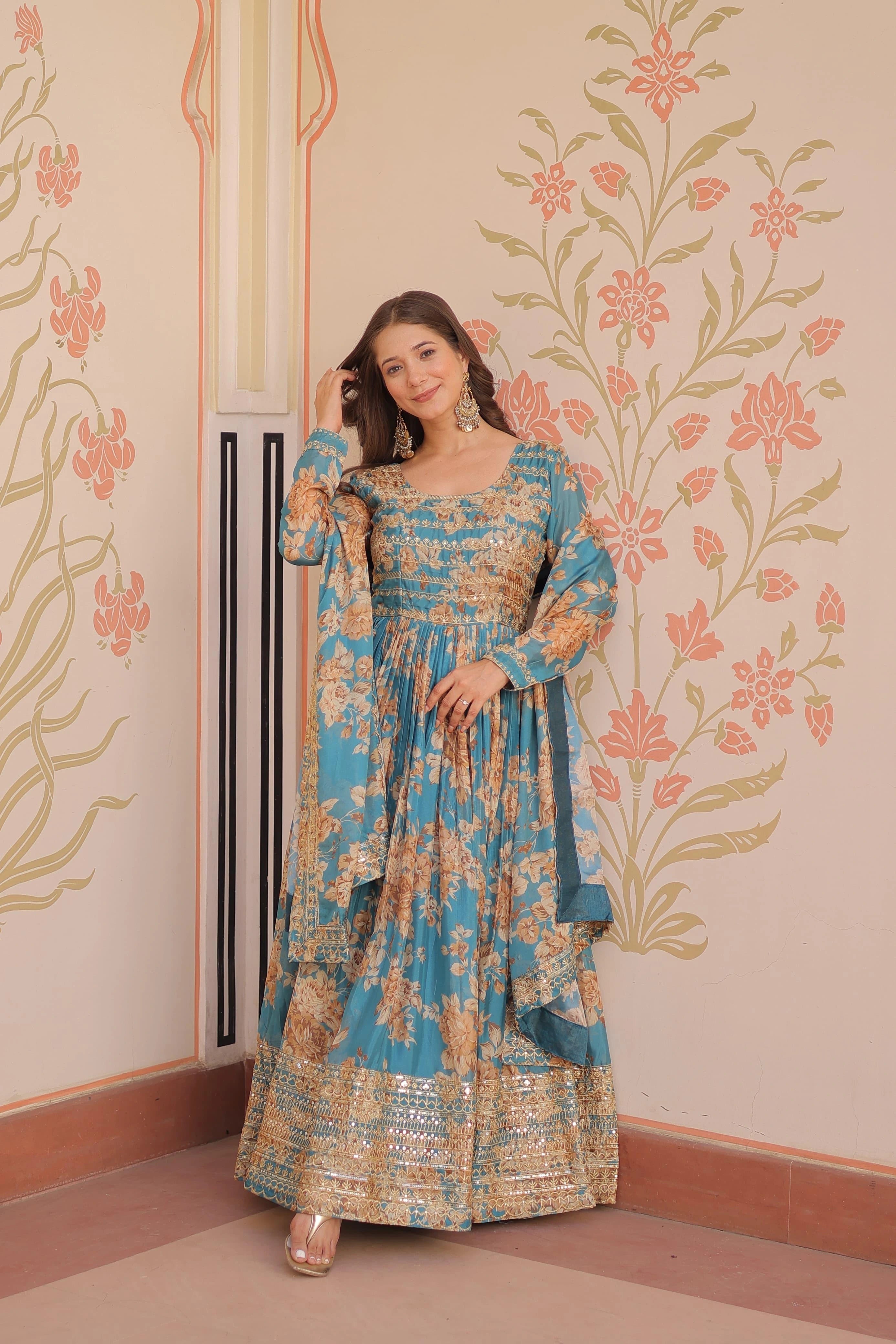 Woman in a blue floral dress standing against a decorative wall.