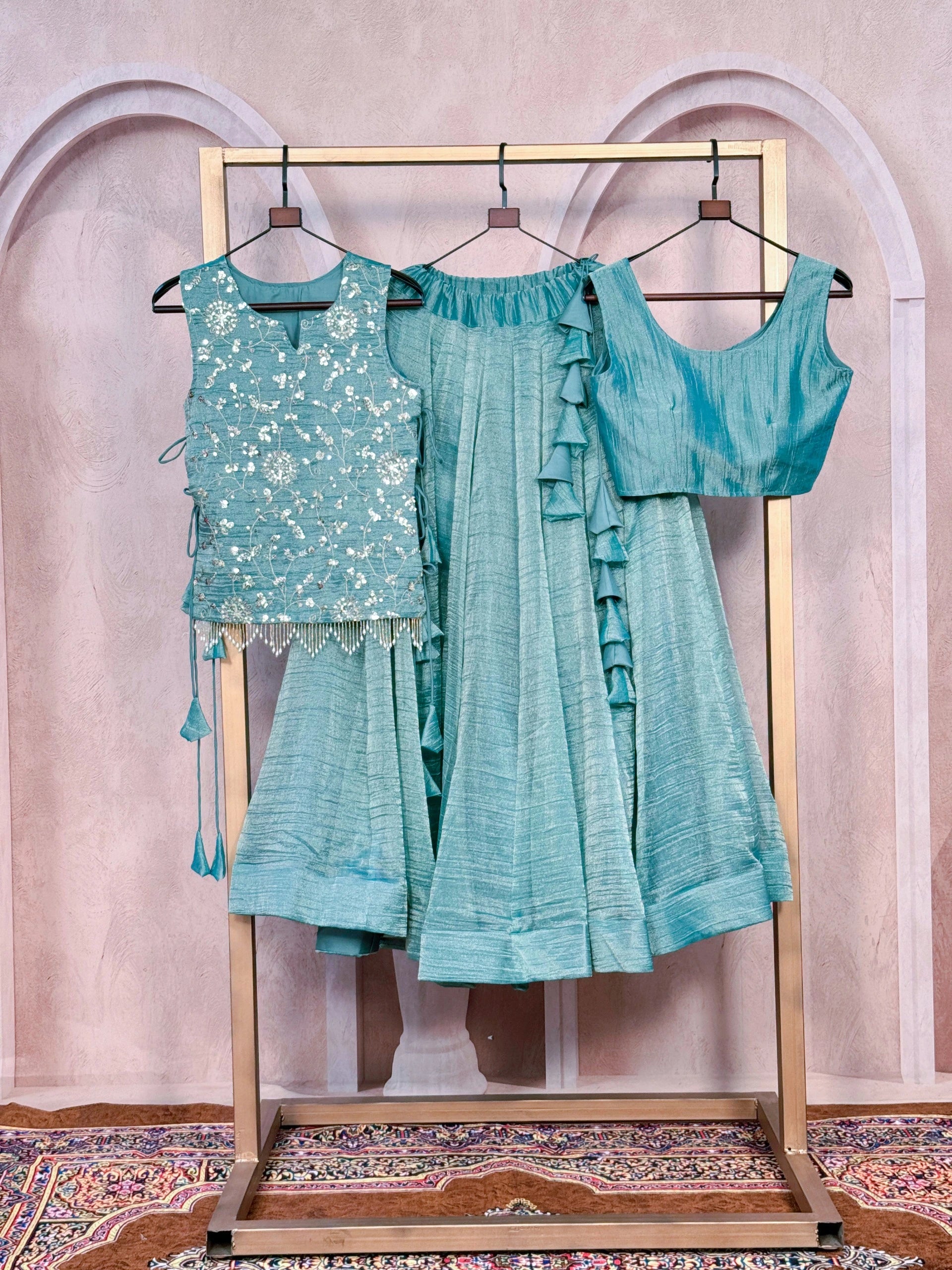 Teal traditional outfit with embroidered top and ruffled dupatta on a stand against a decorative wall.