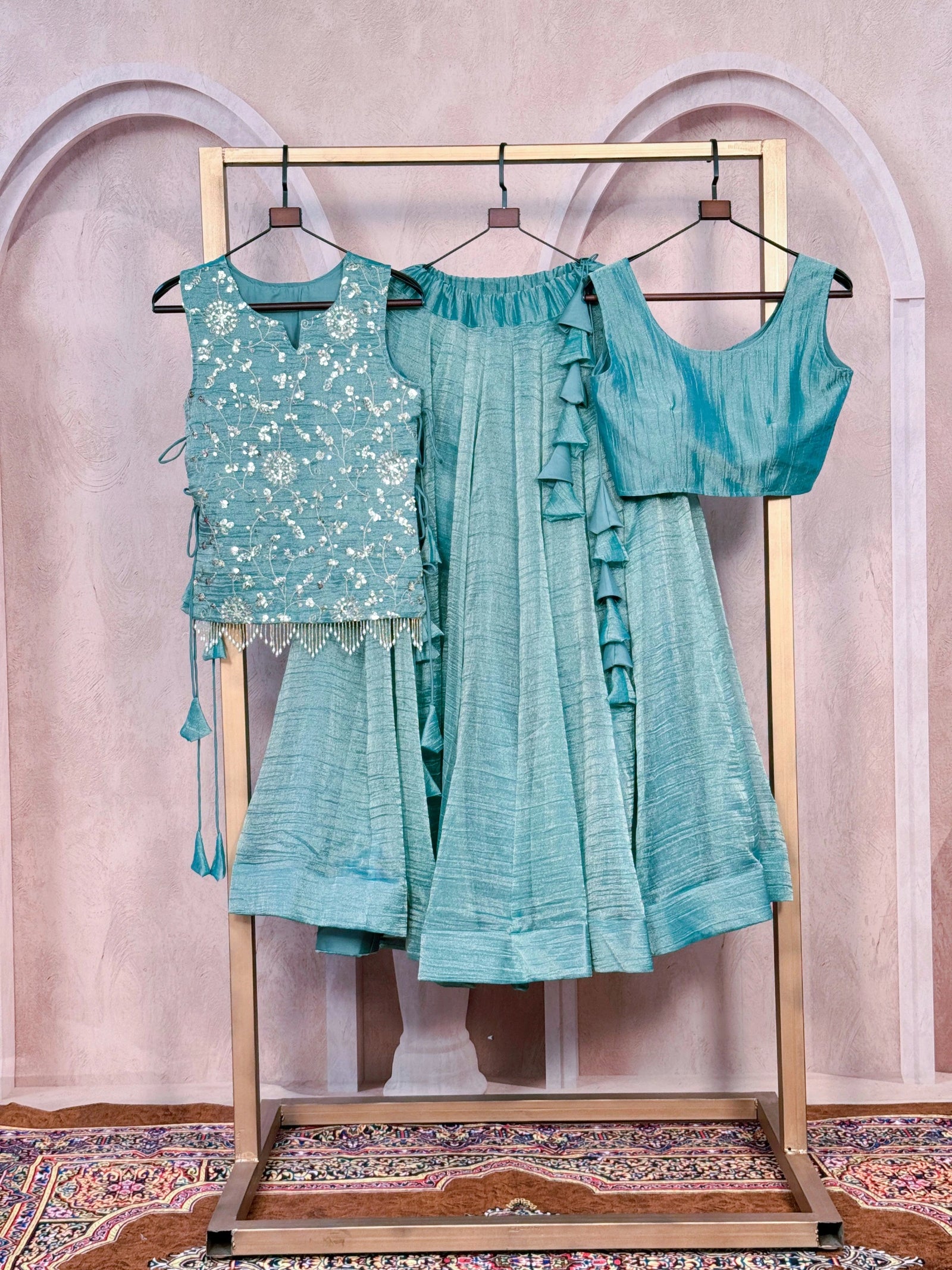 Teal traditional outfit with embroidered top and ruffled dupatta on a stand against a decorative wall.