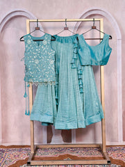 Teal traditional outfit with embroidered top and ruffled dupatta on a stand against a decorative wall.