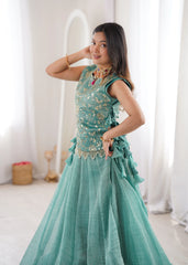Woman in a teal dress with gold embellishments posing in a bright room.
