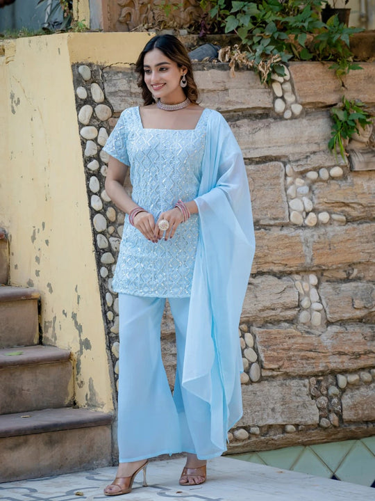 Woman in a light blue traditional outfit standing outdoors against a stone wall.