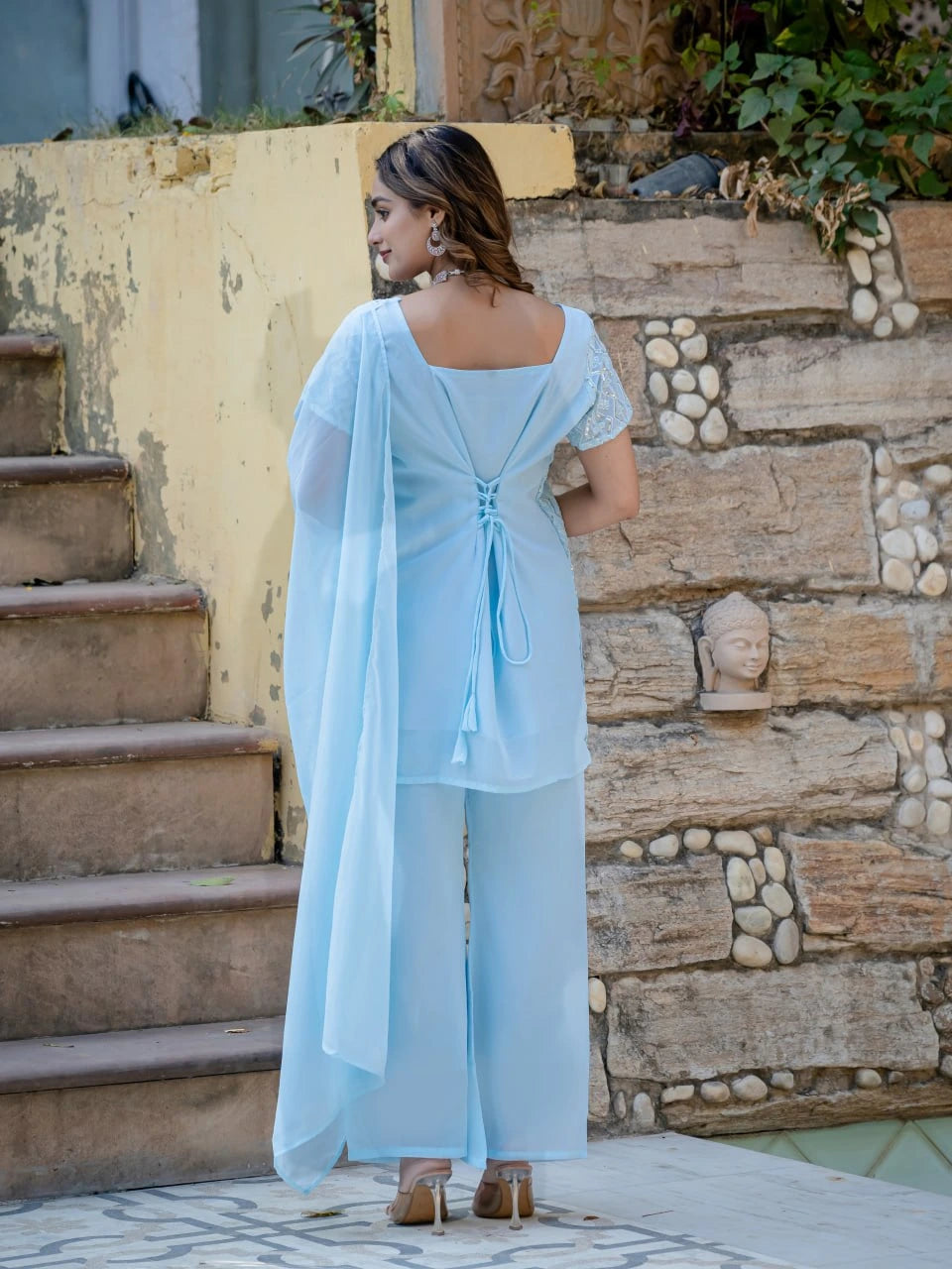 Woman in a light blue outfit standing on stone steps with a stone wall background