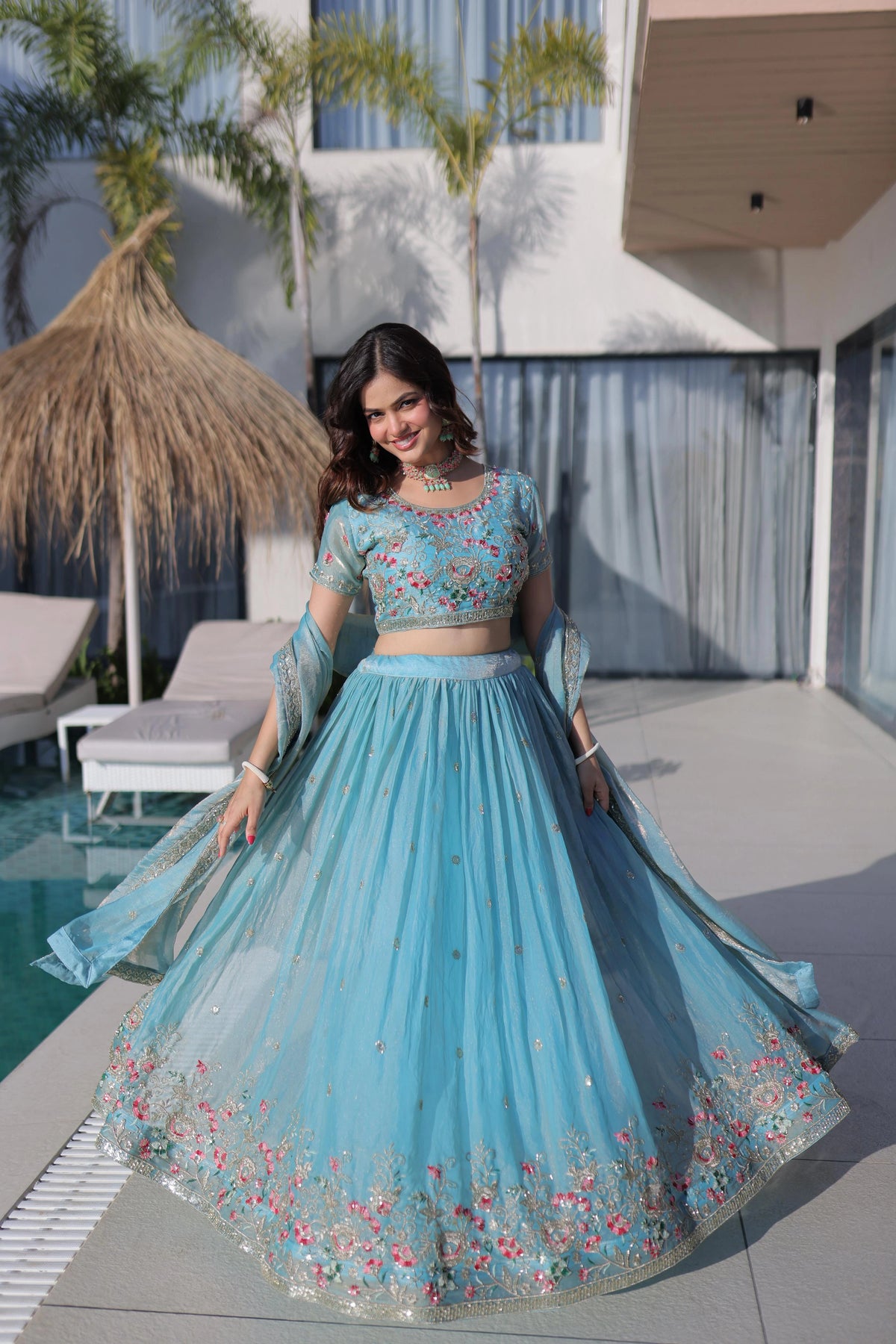 Woman in a blue embroidered traditional outfit standing by a poolside.