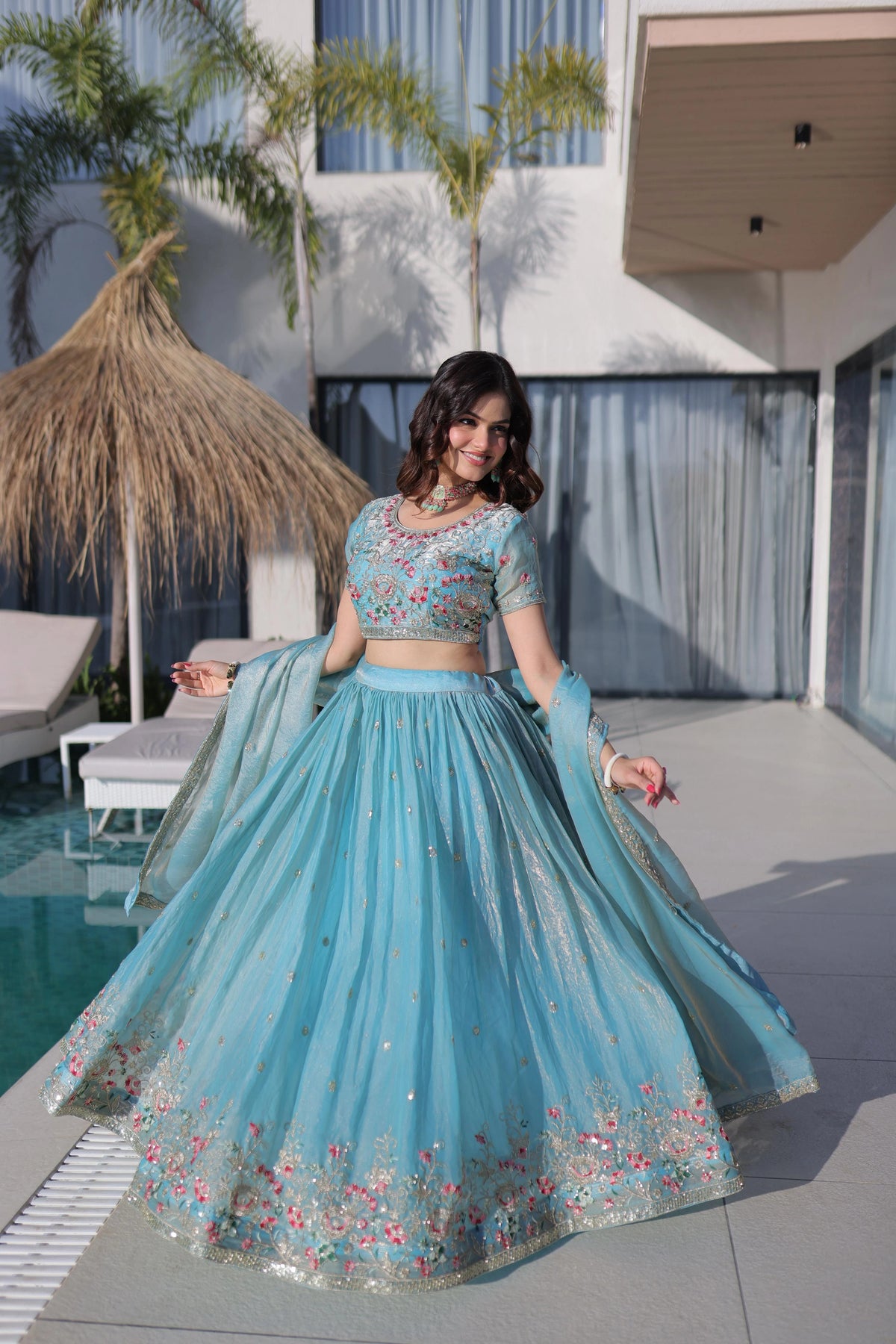 Woman in a blue embroidered traditional outfit by a poolside.
