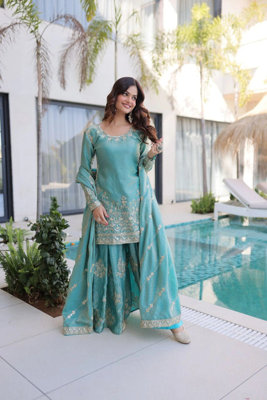 Woman in a turquoise traditional outfit standing by a poolside.