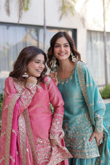 Two women in traditional pink and blue embroidered dresses standing outdoors.