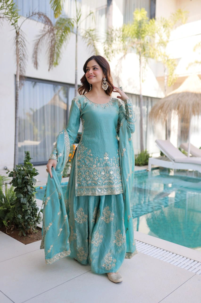 Woman in a turquoise traditional outfit standing by a poolside.