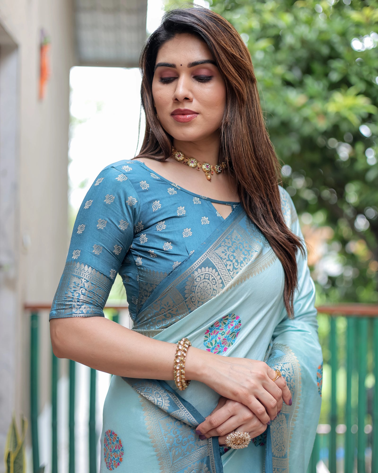 Woman wearing a light blue saree with a blurred green outdoor background