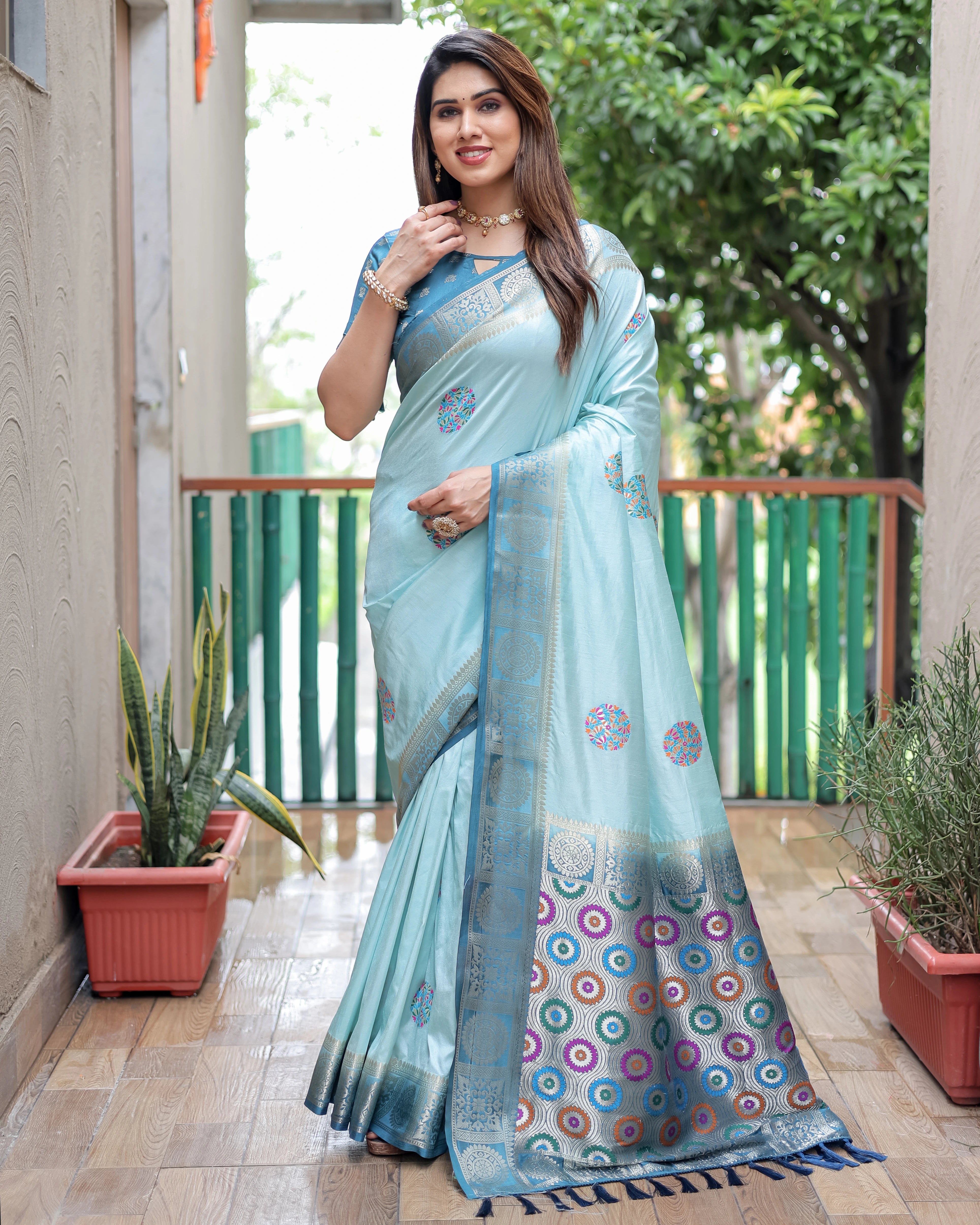 Woman wearing a light blue saree with a patterned border on a balcony.
