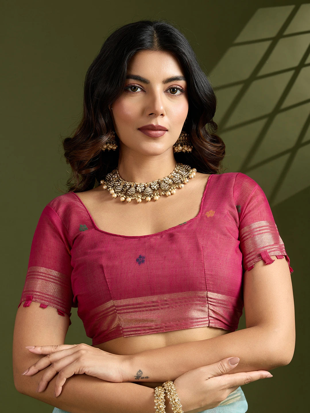 Woman wearing a pink blouse with gold jewelry against a green background